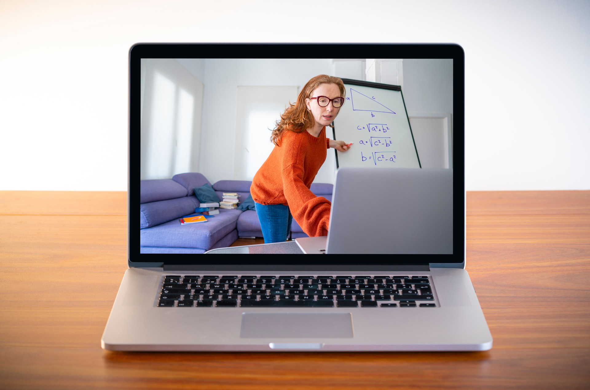Female teacher teaching remotely her class from laptop screen on wood