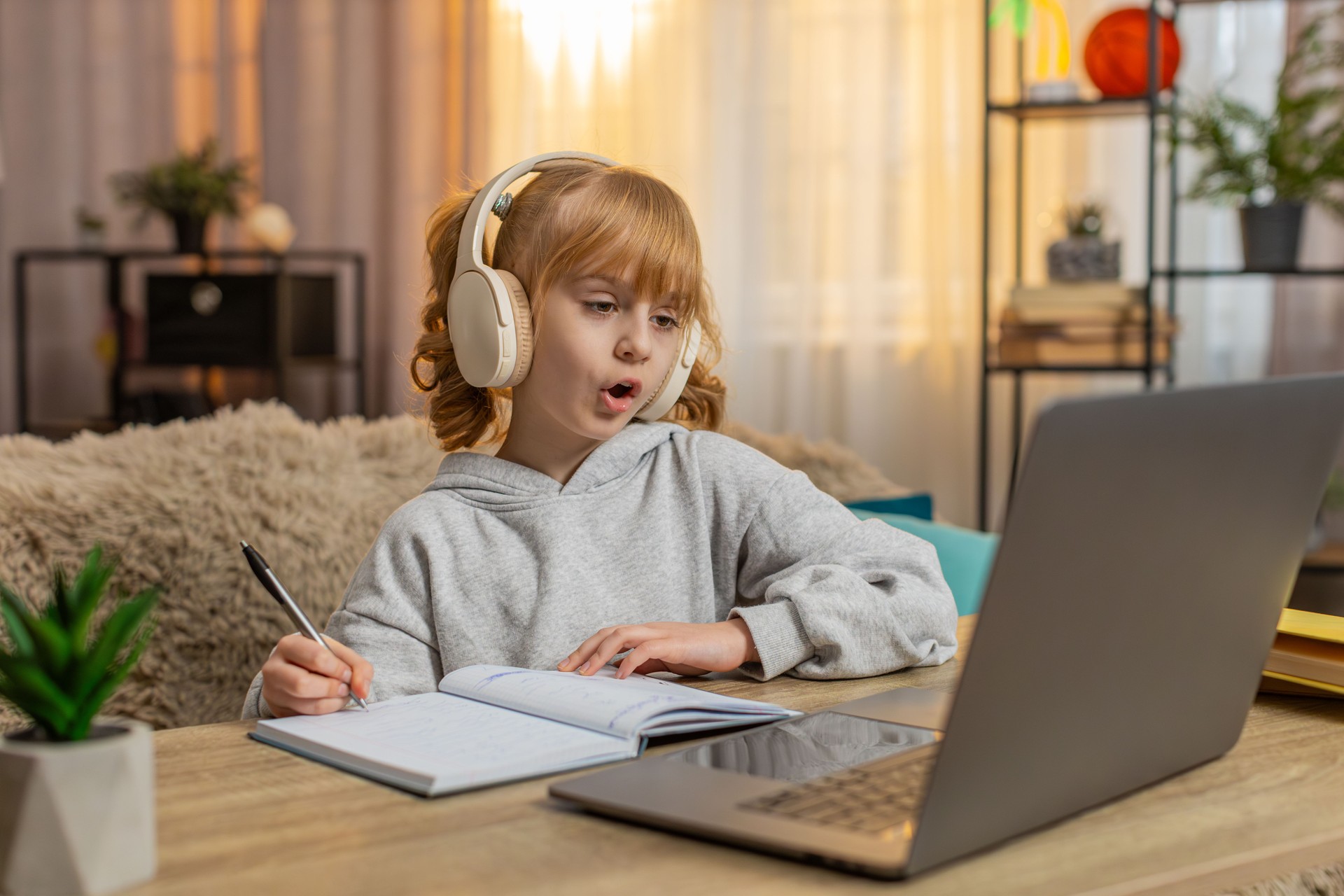 Young girl wearing wireless headphones learning English with audio lesson repeating new words aloud